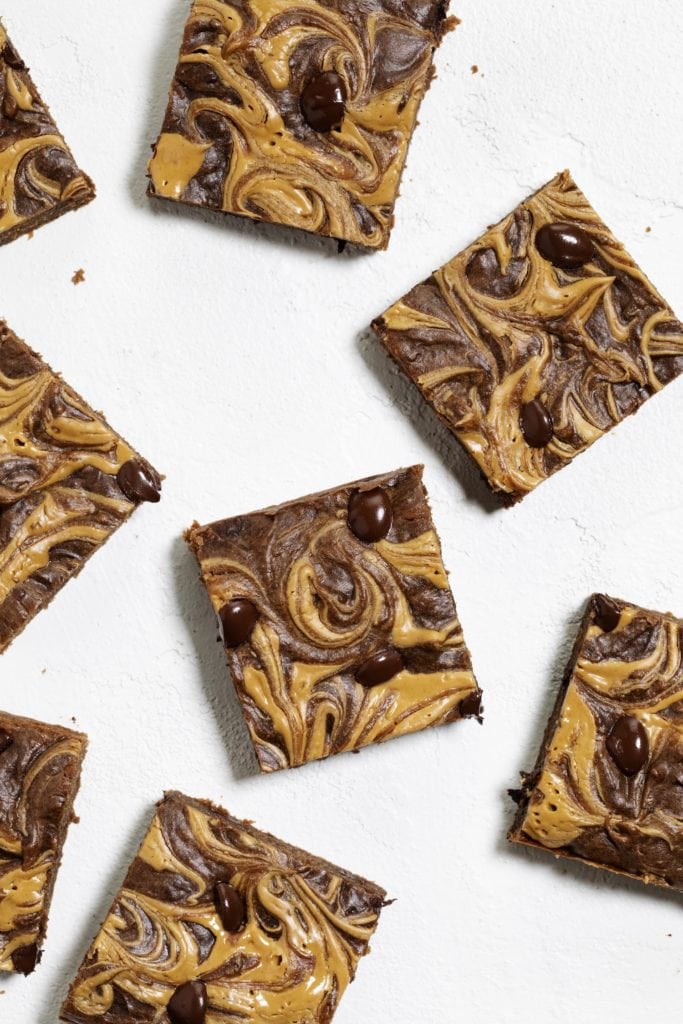 Peanut butter swirled brownies on a white surface.