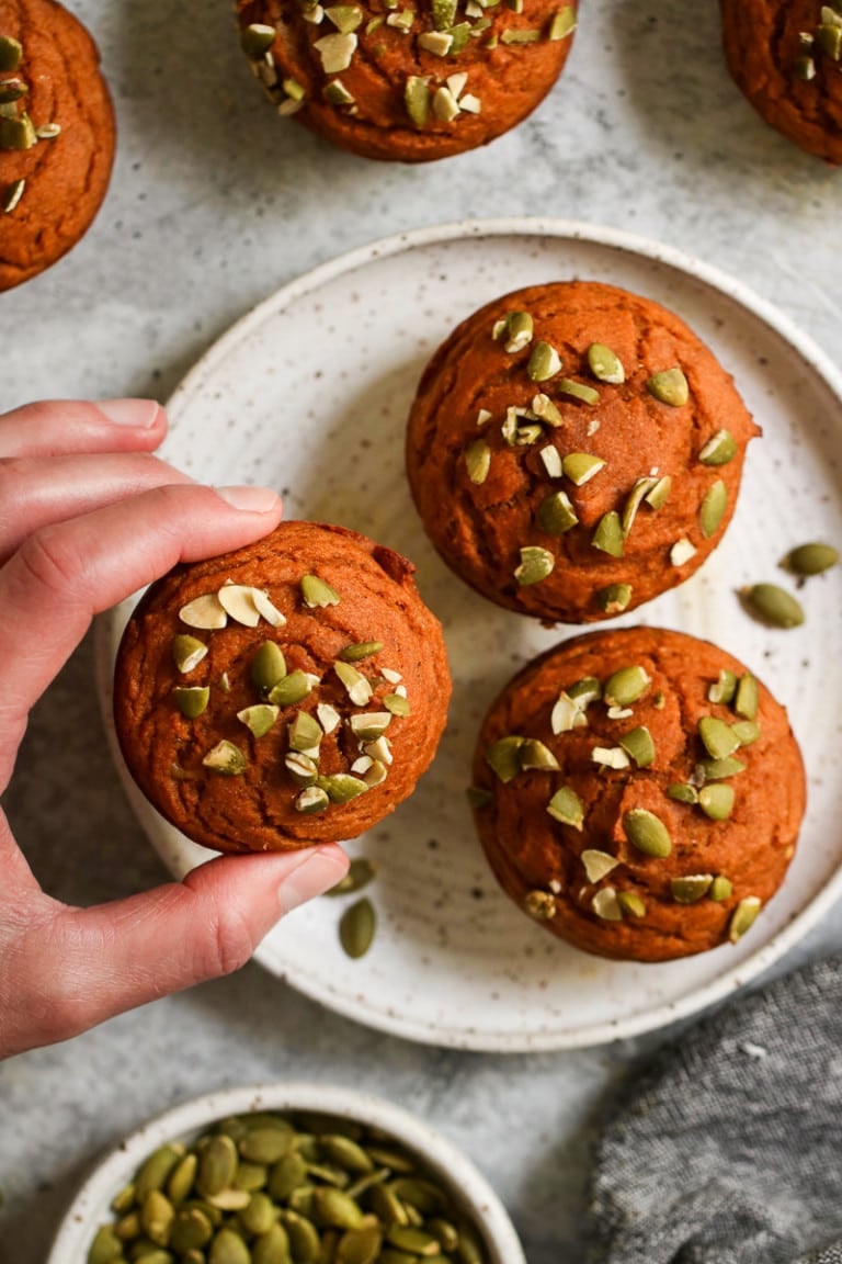 Overhead view of a plate of three pumpkin protein muffins with pepitas on top. 