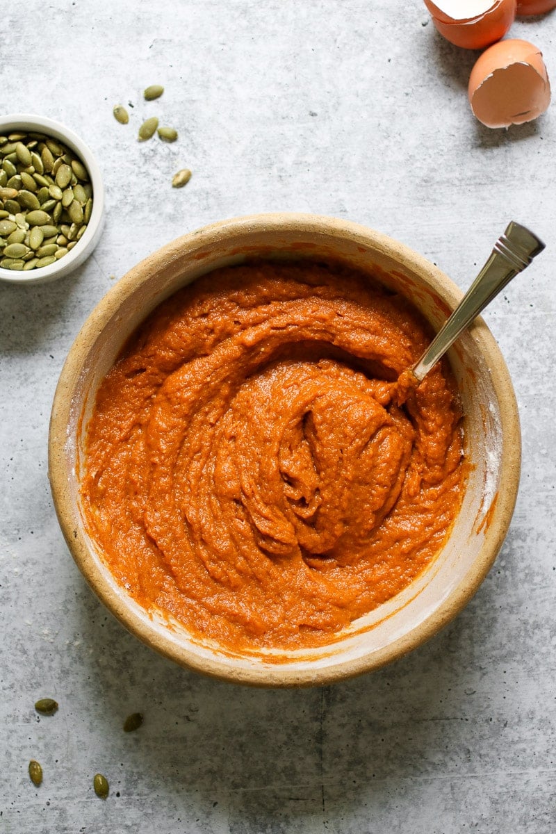 Overhead view of a bowl of pumpkin puree with a spoon handle sticking out of the bowl. 