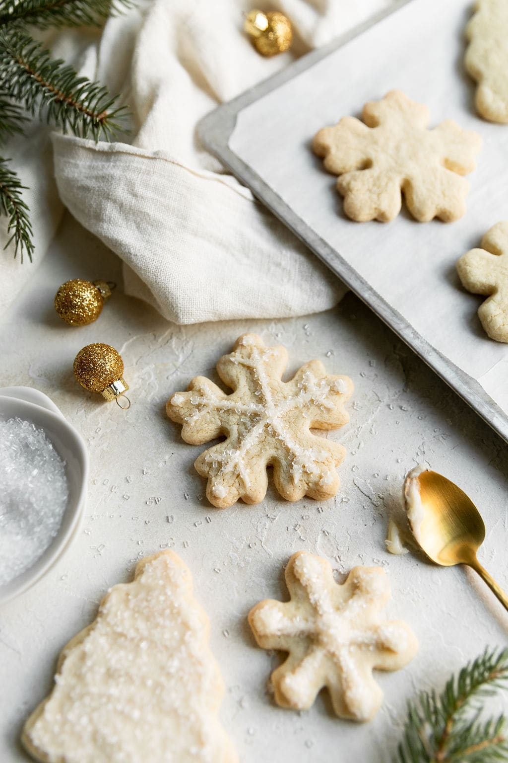 A gluten-free sugar cookie cut-out in a snowflake with minimal white piping on cookie next to a baking sheet with freshly baked cookies lined up.