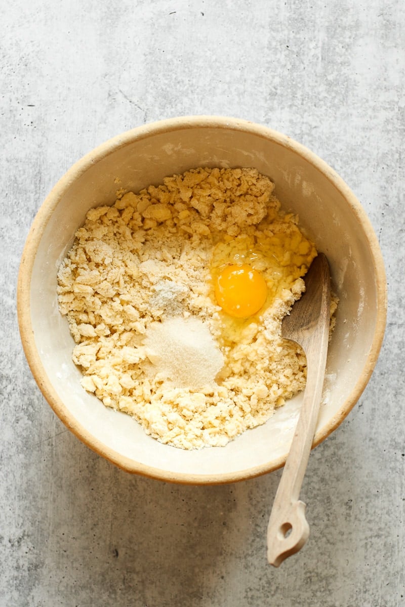Gluten-free pie crust dough in a mixing bowl with sugar and an egg in the mixing bowl.