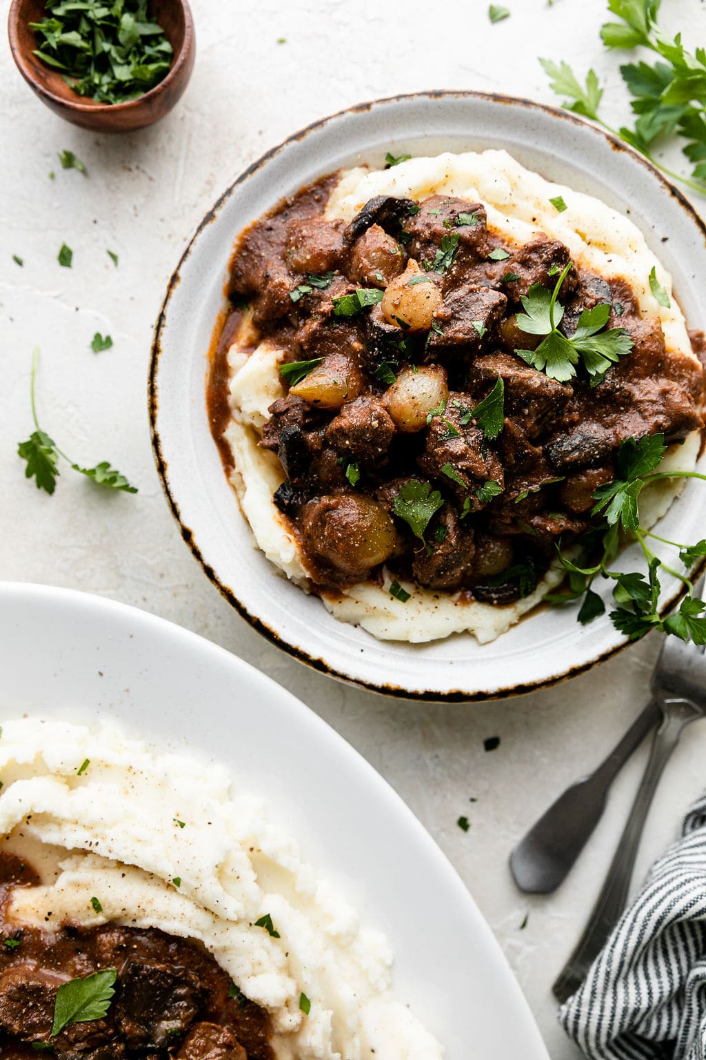 Overhead view of beef tips and gravy plated over a high pile of creamy mashed potatoes and garnished with fresh herbs.