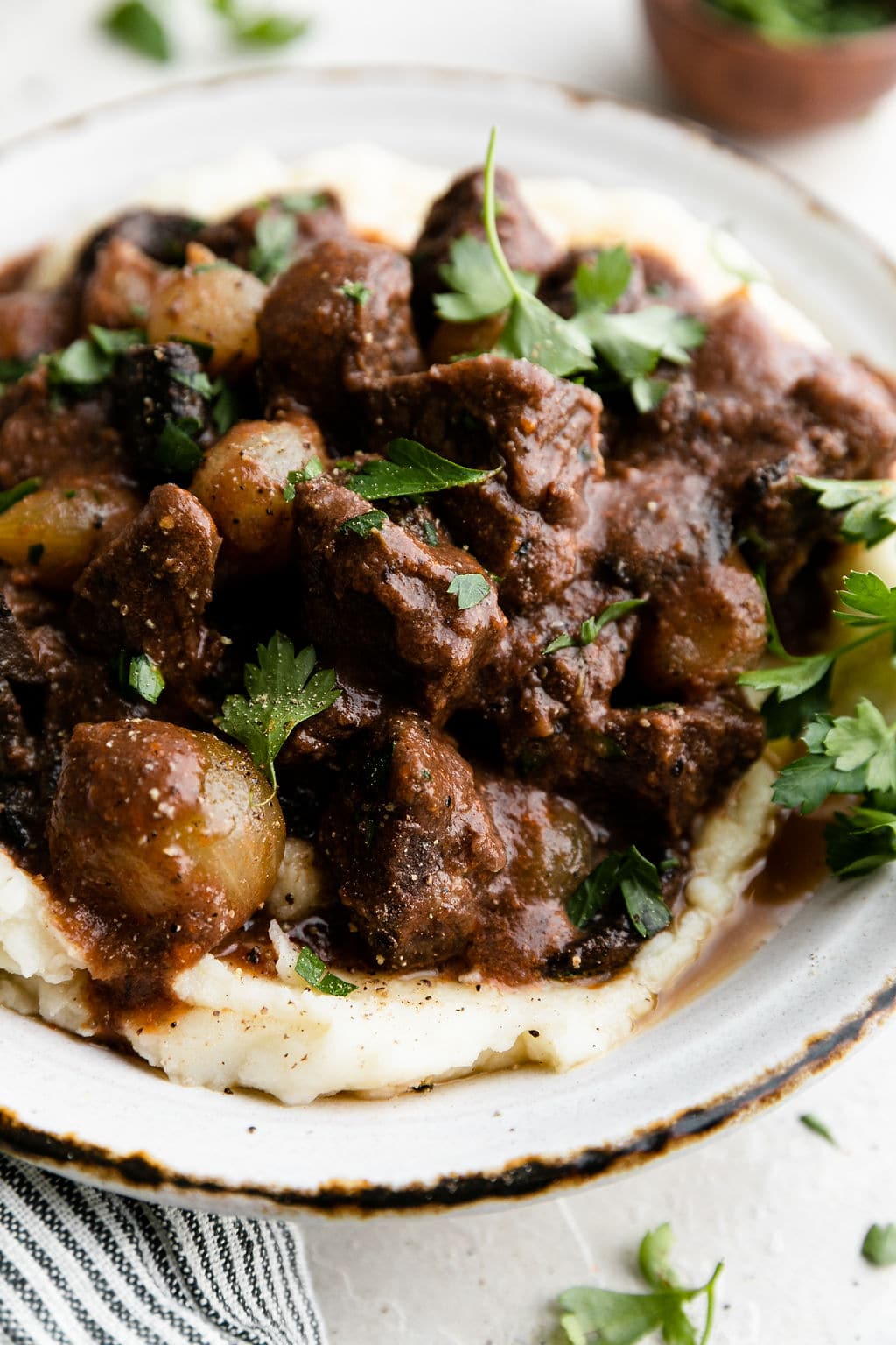 Close up view of big chunks of slow cooked beef tips coated in gravy with pearl onions mixed in and served over mashed potatoes.
