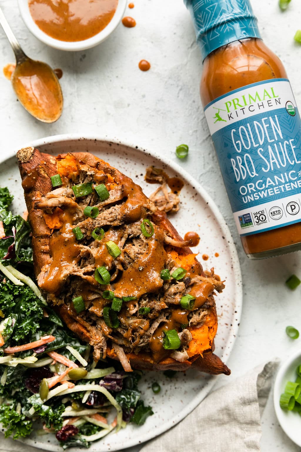 A shredded pork stuffed sweet potato topped with honey mustard bbq sauce with a jar of Primal Kitchen Golden BBQ Sauce on the side.