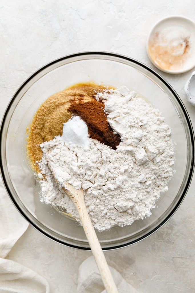 All ingredients for gluten-free Snickerdoodles in a mixing bowl with a wooden spoon.
