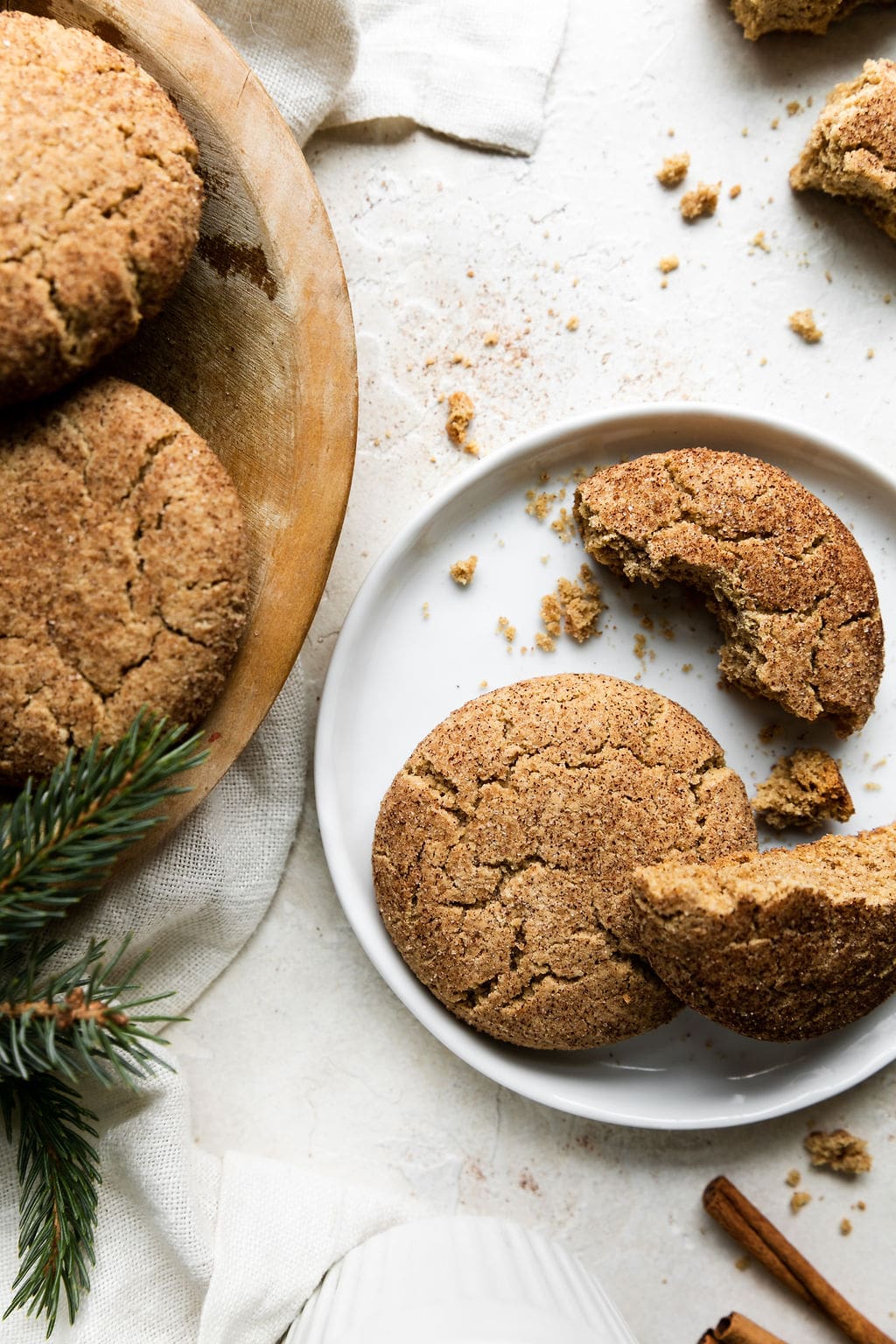Two gluten free snickerdoodle cookies on a small white plate; one cookie broken in half to show texture.