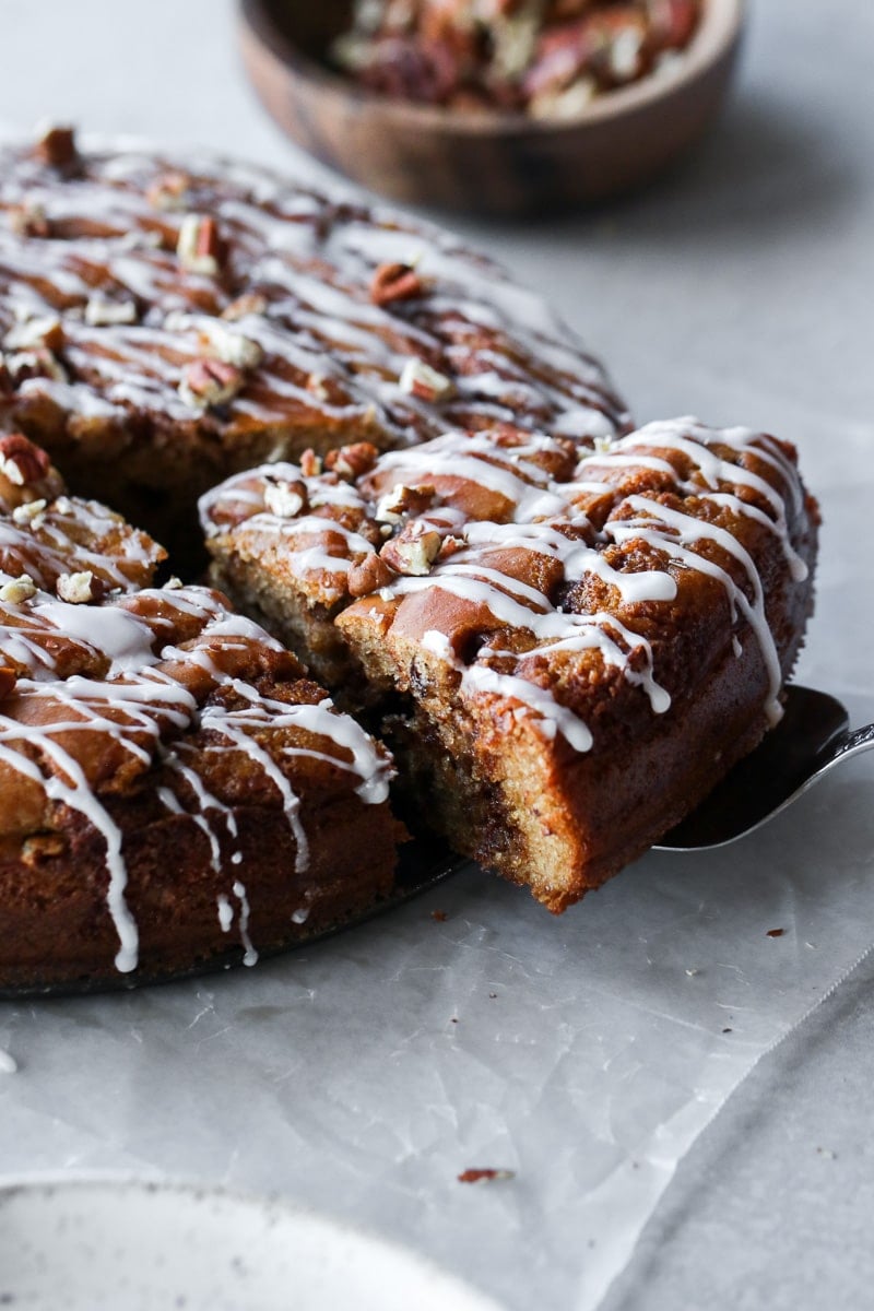 A slice of cinnamon roll coffee cake being lifted from the round cake, topped with white drizzle.