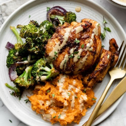 Overhead view of chipotle chicken thigh plated on a white plate with side of broccoli and mashed sweet potatoes, drizzled with honey mustard sauce.