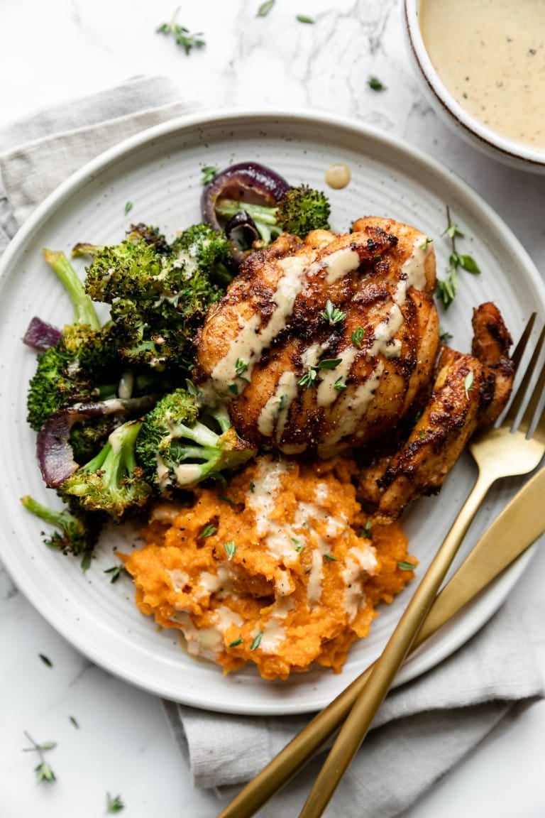 Overhead view of a plate filled with roasted broccoli, mashed sweet potatoes, and a chicken thigh topped with honey mustard sauce. 