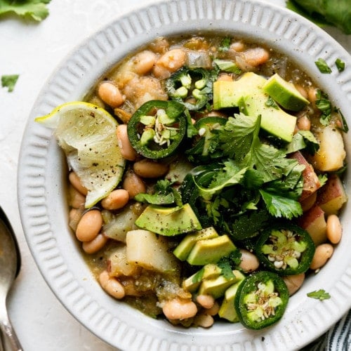 Close up overhead view of slow cooker green chile stew with white beans and potatoes in a white bowl