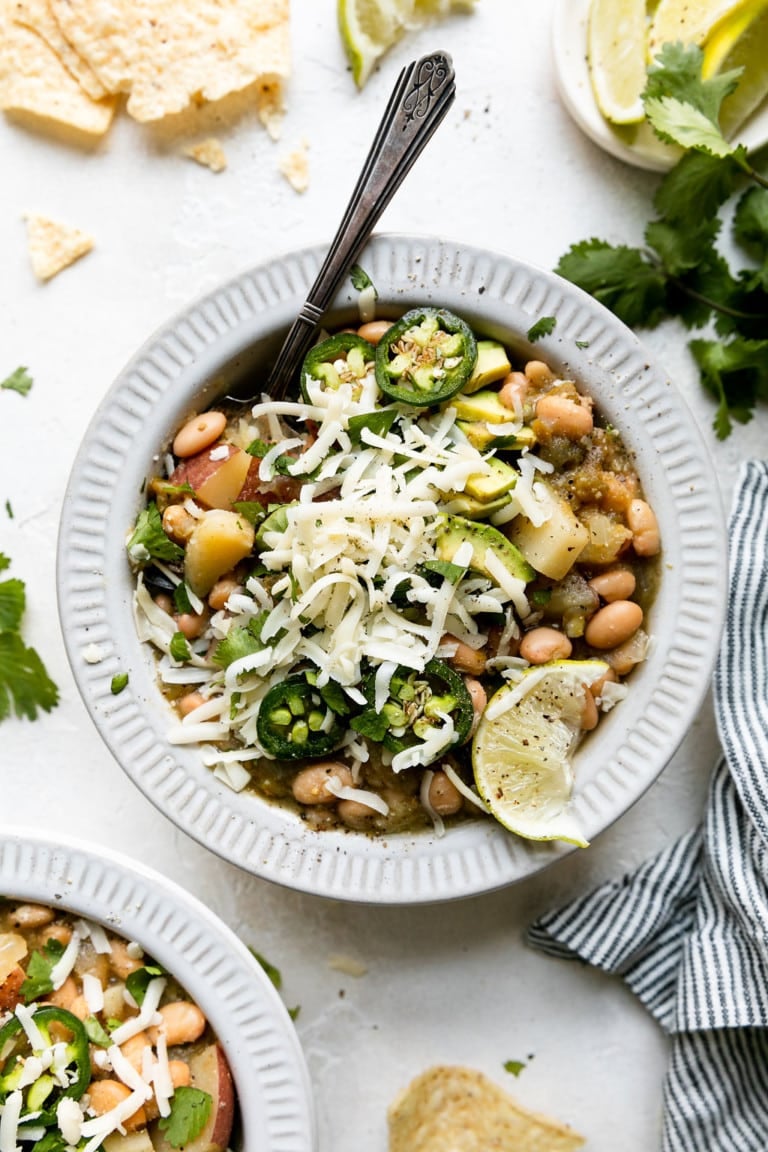 Overhead view of a bowl of green chili stew with beans and topped with shredded cheese. 