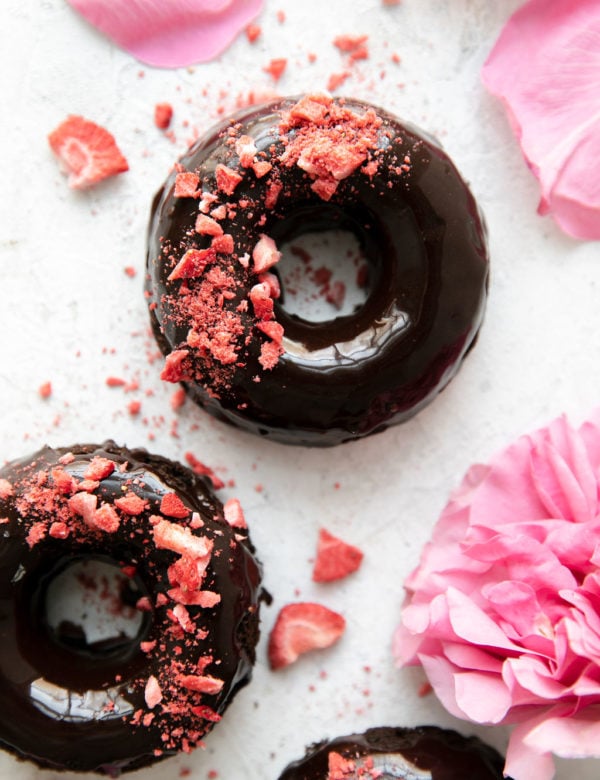 Chocolate covered chocolate donuts on a counter sprinkled with red dried strawberry pieces
