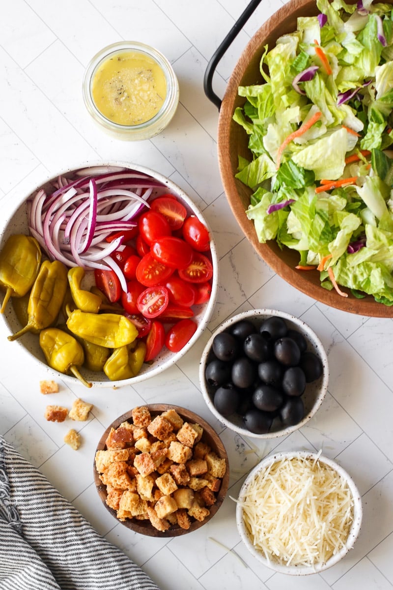 Overhead view of ingredients for a copycat Olive Garden salad arranged together in separate bowls. 