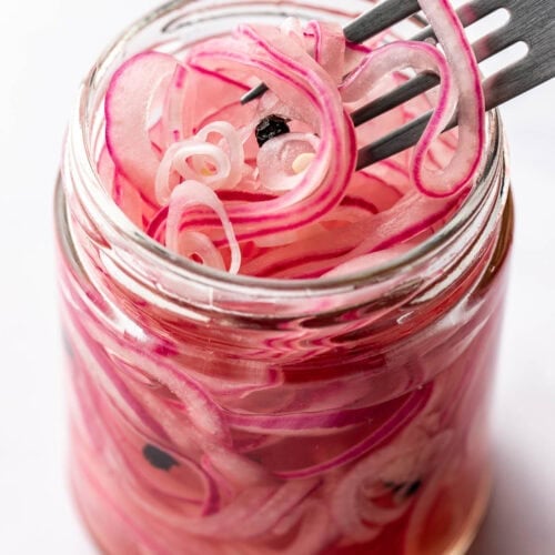 Close up view of a jar of Quick Pickled Onions and a fork bringing out some slices showing the bright purple color.