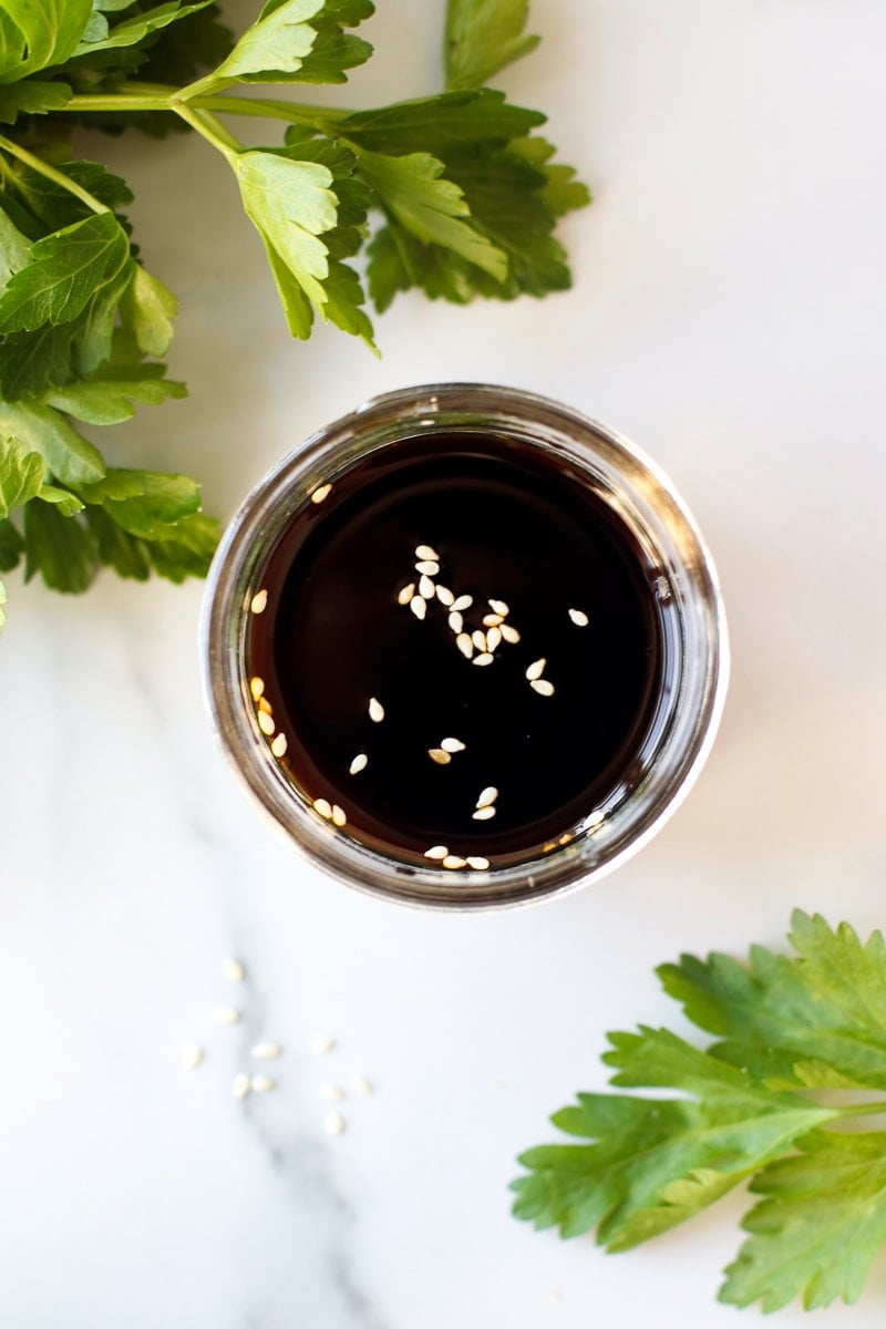 Overhead view of a small jar of dark coconut aminos with a few sesame seeds sprinkled on top.