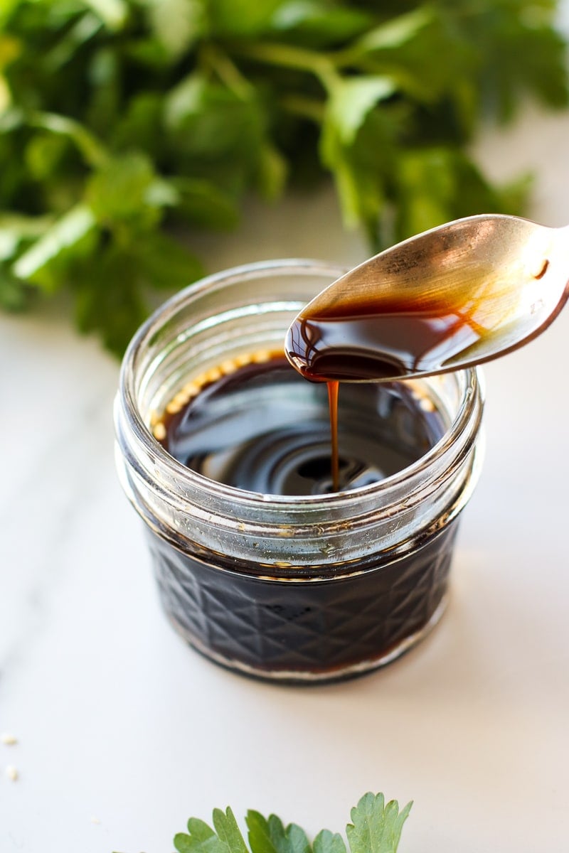 A spoon pouring a spoonful of coconut aminos into a short jar filled with coconut aminos