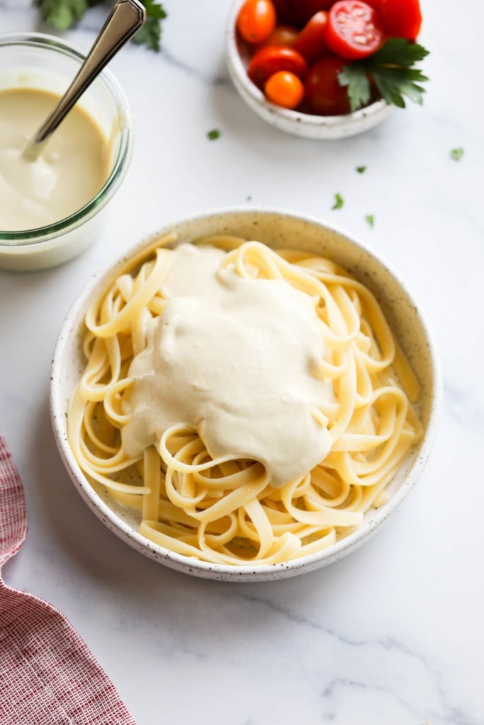 A bowl of pasta with freshly drizzled Vegan Alfredo Sauce on top
