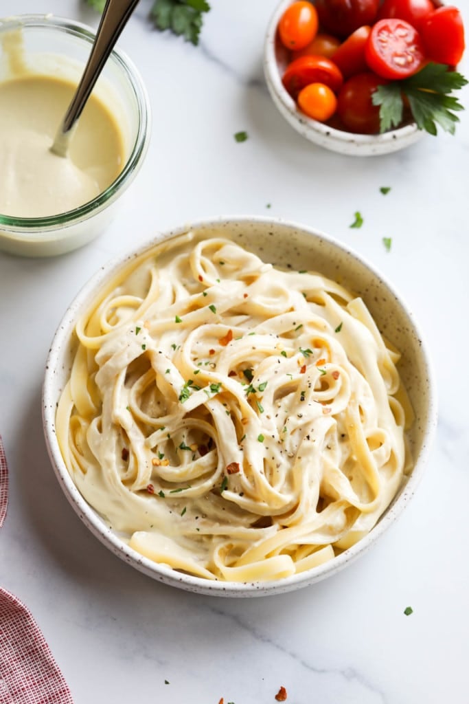 Overhead view of a bowl of pasta next to a bowl of Vegan Alfredo Sauce
