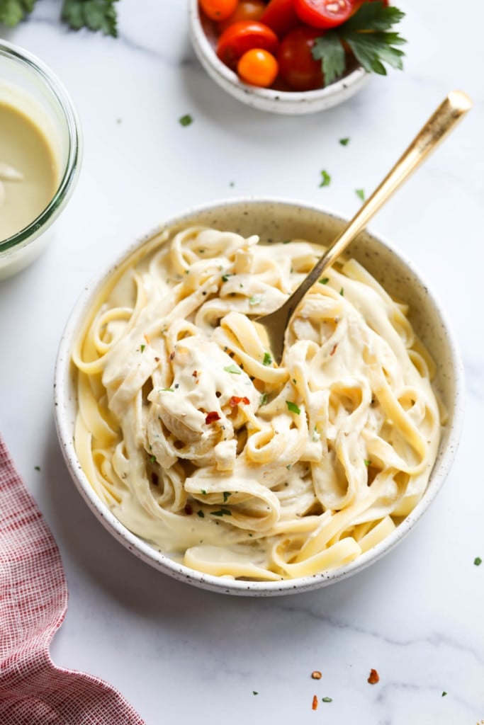 Overhead view of a bowl of alfredo noodles and Vegan Alfredo Sauce on top with fresh herbs and seasonings
