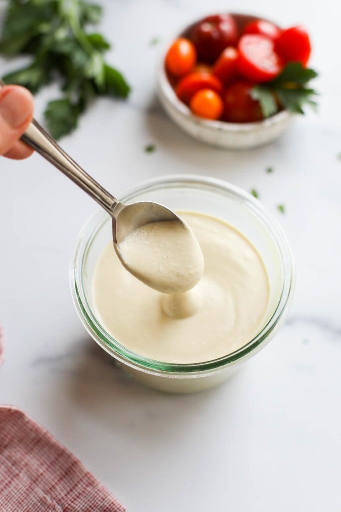A spoon scooping a spoonful of Vegan Alfredo Sauce from a jar to show the creamy texture