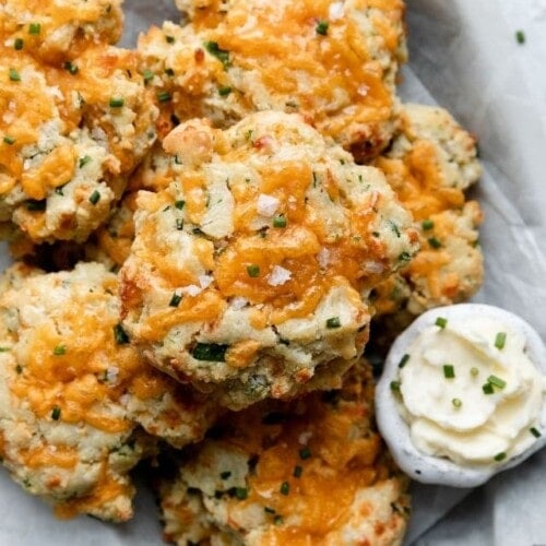 Gluten-free Garlic Cheddar Biscuits in a pile in a parchment-lined serving tray, a side of whipped butter.