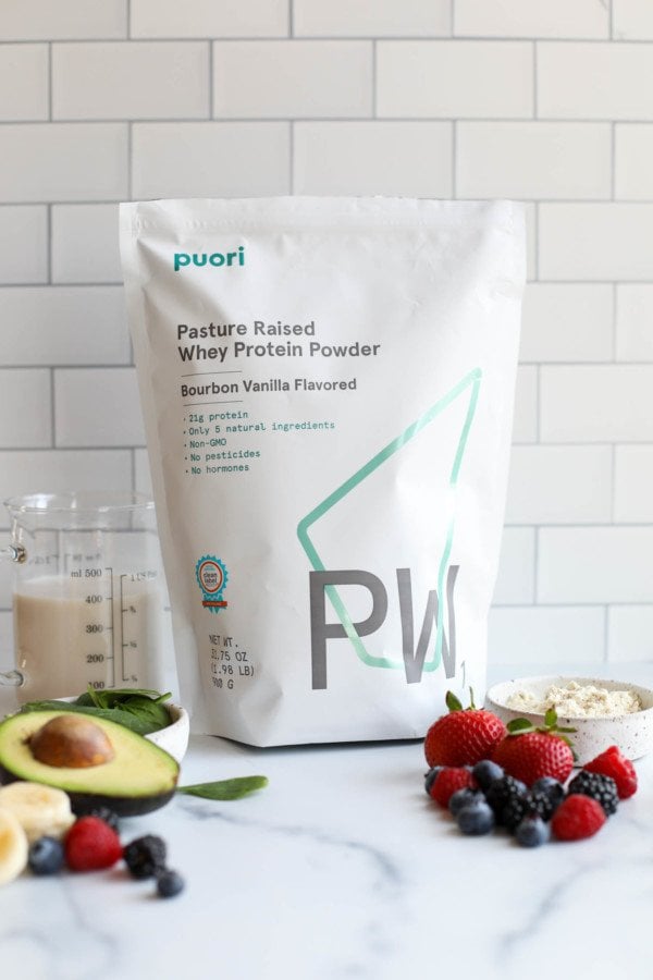 A bag of protein powder on a marble countertop with fruit in front of the bag.