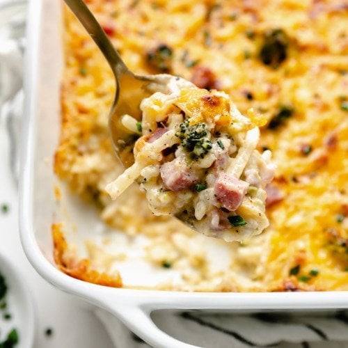 A spoonful of cheesy scalloped potatoes and ham being scooped from baking dish