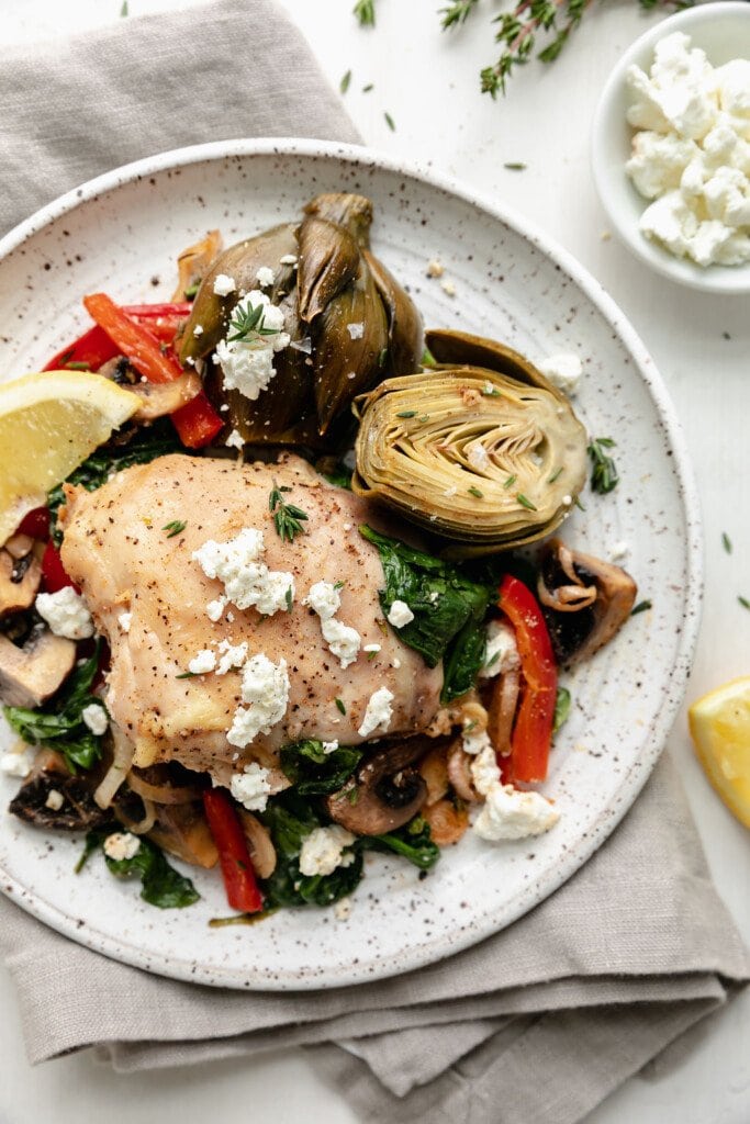 Sheet pan artichoke chicken with extra veggies served on a speckled plate sprinkled with feta cheese.