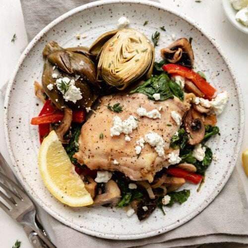 Sheet pan artichoke chicken with goat cheese served on a speckled plate