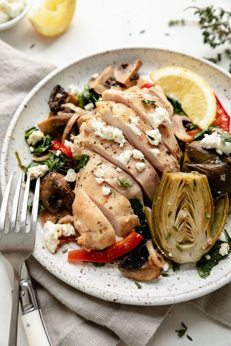 Sheet pan artichoke chicken and veggies with goat cheese served on stone plate. 