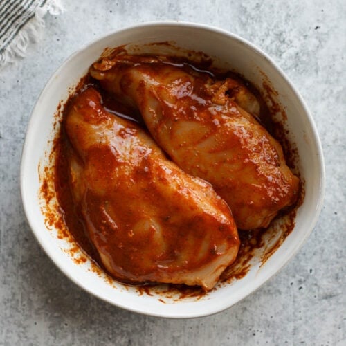 Overhead view of two chicken breasts in a white bowl marinating in chicken fajita marinade.