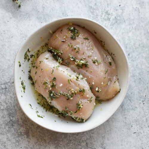 Overhead view of lemon herb chicken marinade in a white bowl with two chicken breasts.