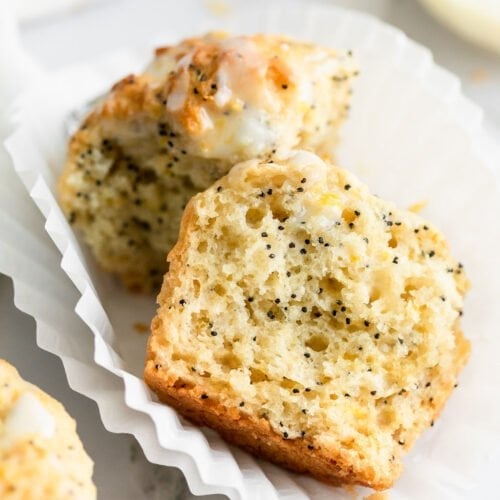A single lemon poppy seed muffin broken in half sitting on two white muffin liners to show inside texture.