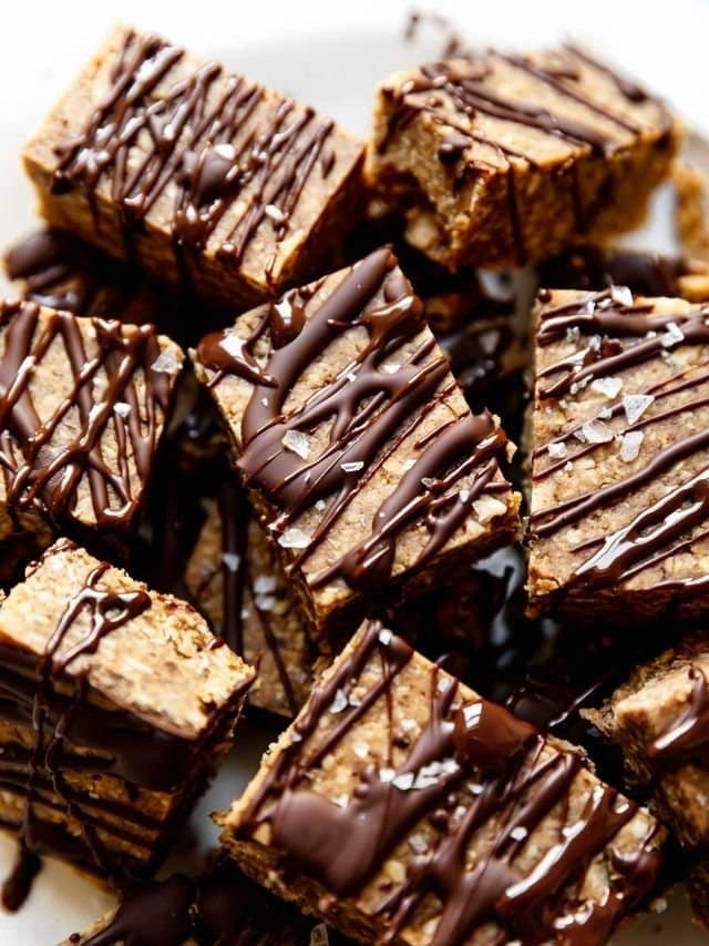 Overhead view of mini peanut butter protein bars in a pile, drizzled with dark chocolate and sprinkled with sea salt flakes.
