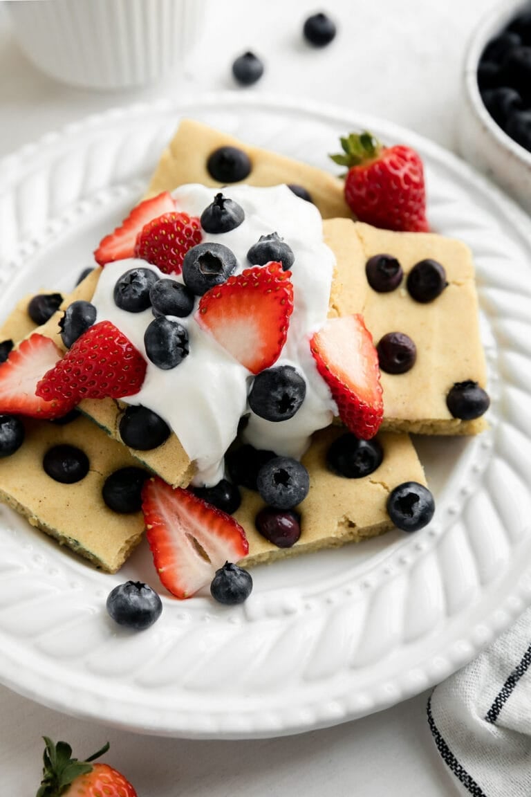 Overhead view of a plate filled with pieces of sheet pan blueberry pancakes topped with fresh fruit and whipped cream