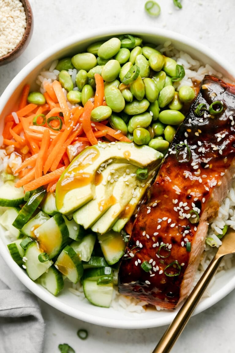 Overhead view of a teriyaki salmon bowl with sliced cucumbers, carrots, avocado, and edamame.