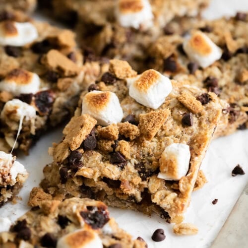 Close up view of square-cut chewy granola bar topped with toasted mini marshmallow perched on another square cut granola bar.