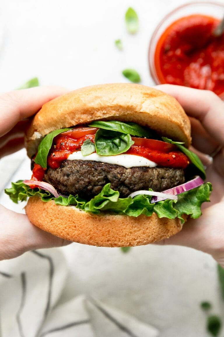 Pizza burger on a bun being held with 2 hands and dipping sauce. 