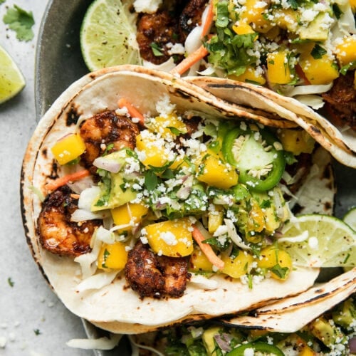 Overhead view of grilled shrimp tacos in double tortillas topped with mango avocado salsa and cojita cheese.