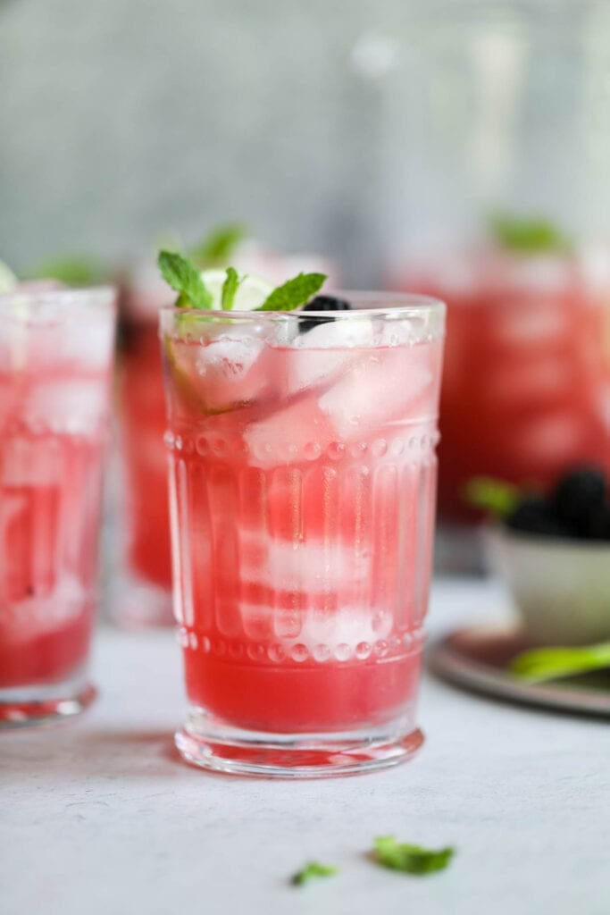 Close up view of a blackberry-lime prosecco cocktail with fresh berries and mint. 