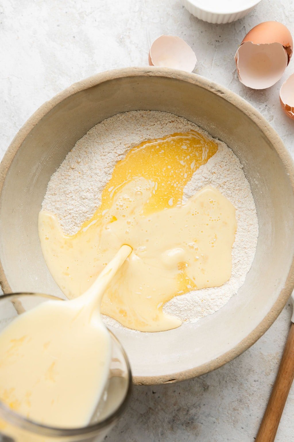 Overhead view of a bowl of dry ingredients for cornbread muffins with the wet ingredients being poured on top.