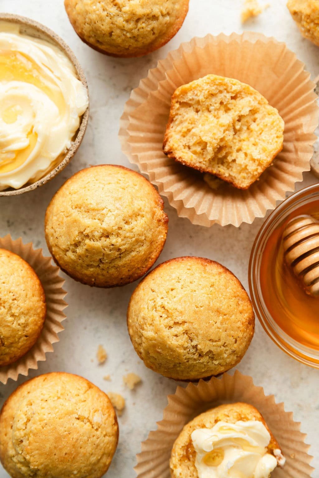 Overhead view of a white countertop filled with Homemade Cornbread Muffins next to a bowl of butter and a dish of honey.
