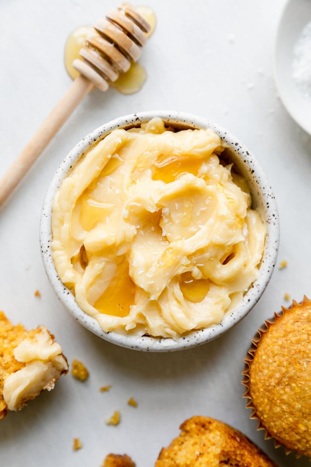 Whipped honey butter in small bowl with honey dipper laying next to bowl.