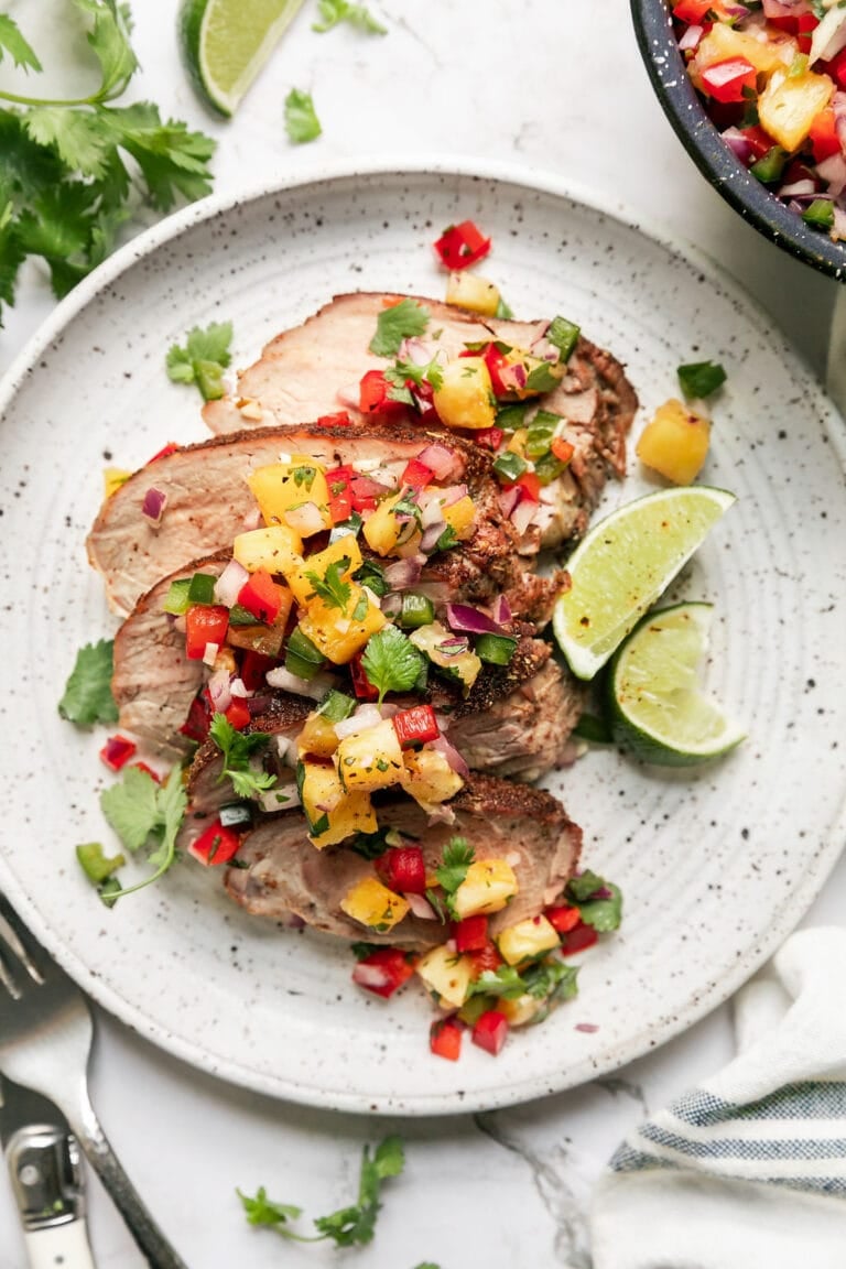 Close up view of a plate of Hawaiian grilled pork tenderloin sliced and topped with a pineapple salsa. 