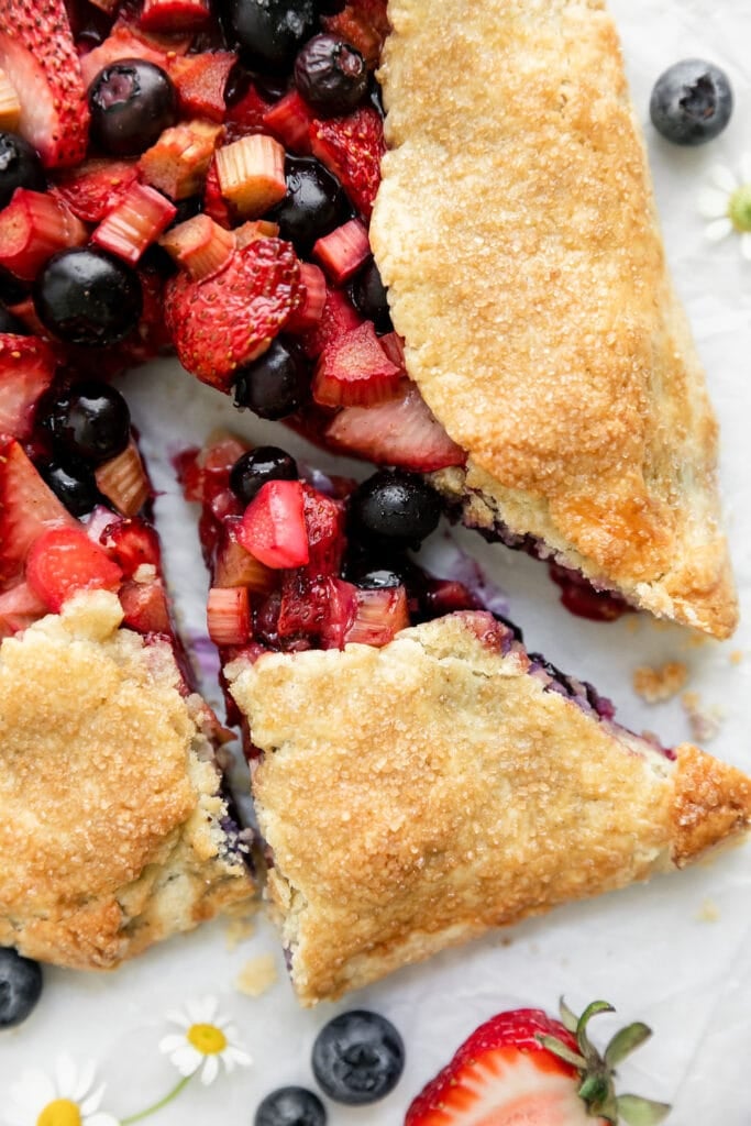 Close up view slice of gluten free strawberry galette with rhubarb slightly removed from entire galette.