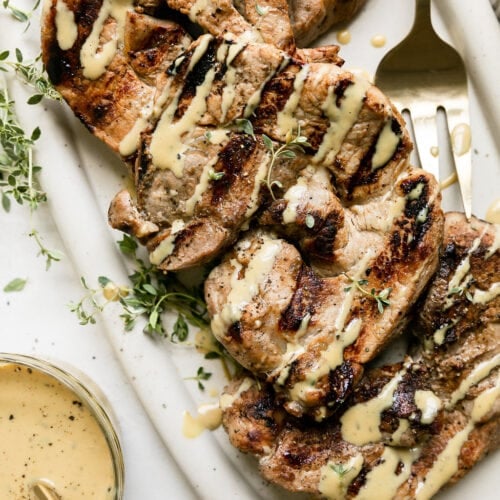 Grilled honey garlic pork chops on white platter drizzled with honey mustard sauce.