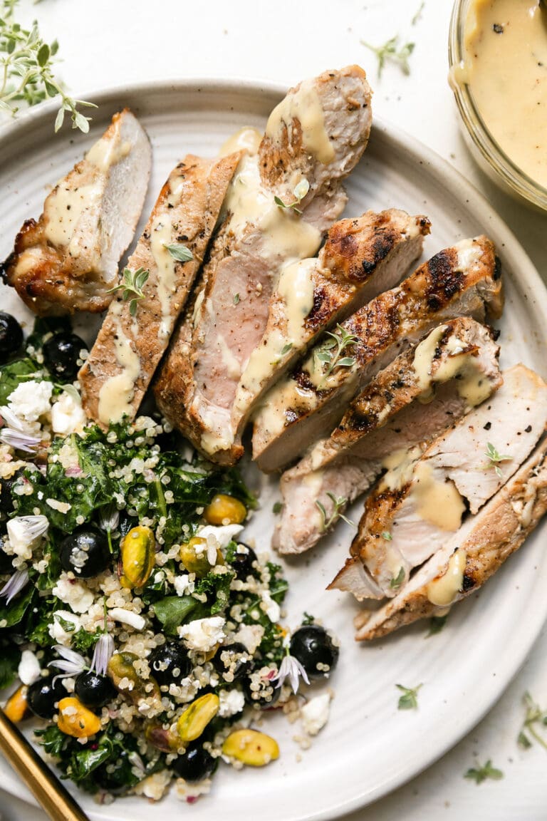 Overhead view of a plate of kale salad with blueberries and a sliced honey garlic grilled pork chop. 