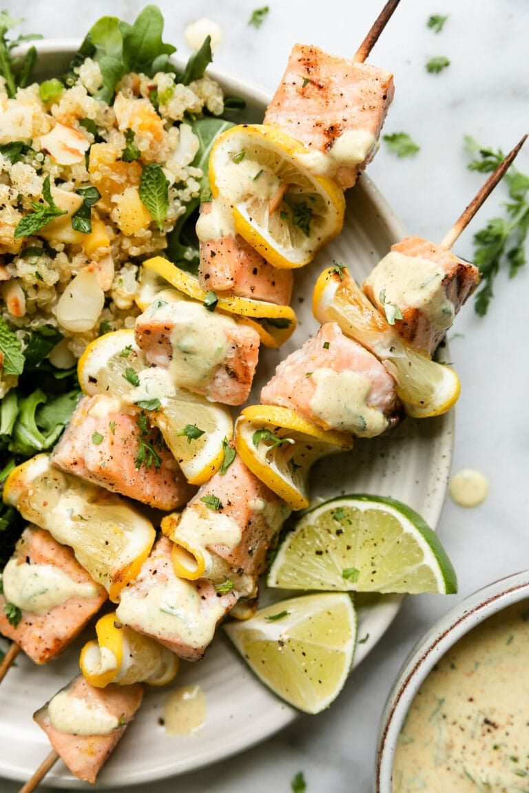 Overhead view of a plate of grilled salmon kabobs drizzled with a creamy curry yogurt sauce and garnished with lime wedges. 