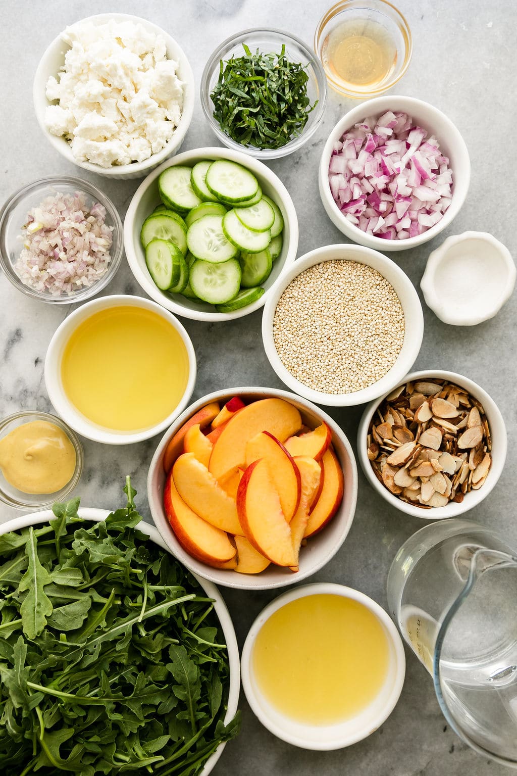 All ingredients for quinoa arugula salad with peaches and goat cheese arranged in small bowls.