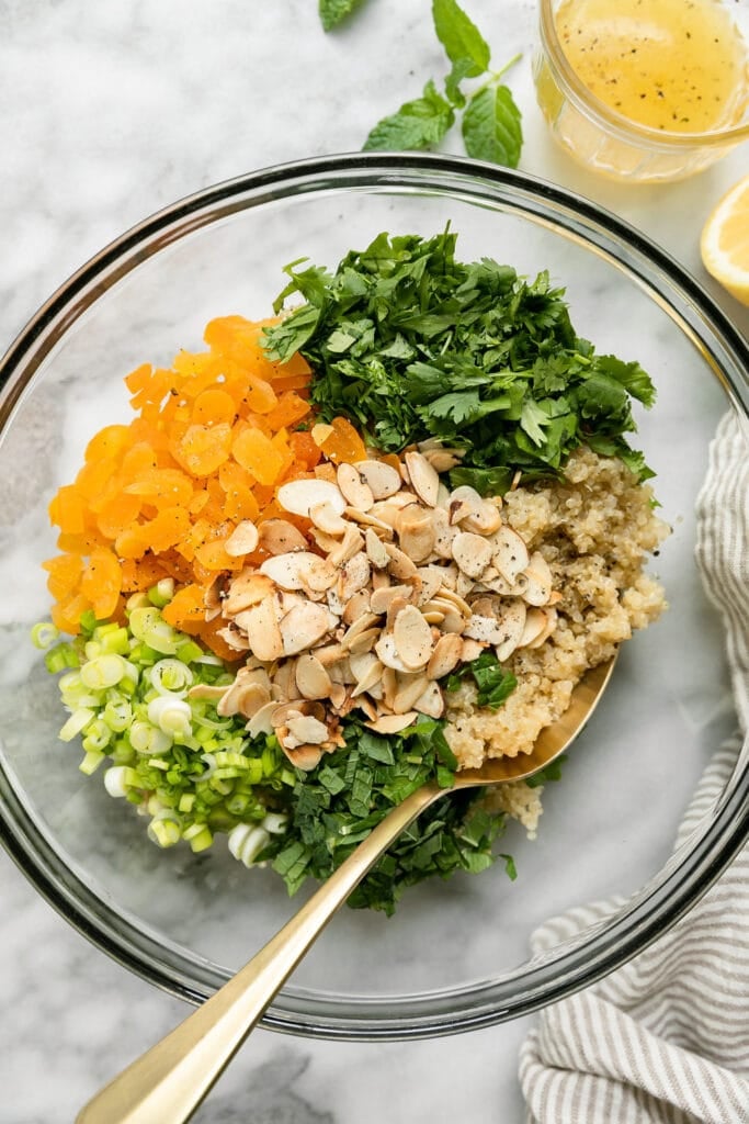 Overhead view clear glass bowl filled with ingredients for herbed quinoa pilaf.